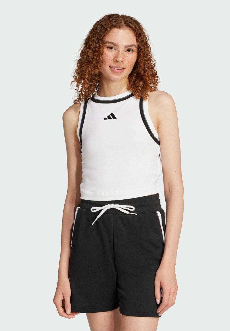 Top corto bianco con bordo nero e logo Adidas, abbinato a pantaloni shorts neri con coulisse e accenti bianchi.