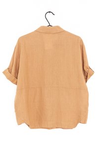 Chemise à manches courtes beige en tissu léger. Elle présente un col, des manches retroussées et un ourlet incurvé à l'arrière.