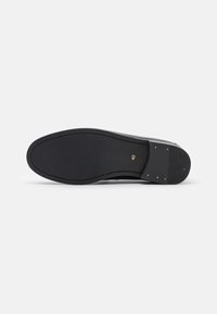 Suela de zapato negra con una superficie de goma suave, ligera textura y costura delineada. Se observan un "42" dorado y remaches cerca del talón.