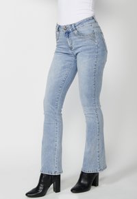 Jeans de denim de color azul claro con una silueta ajustada, ligero acampanado en el dobladillo, remaches decorativos en los bolsillos frontales y diseño de cinco bolsillos.