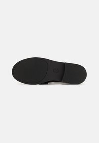 Black shoe sole featuring a textured rubber pattern, rounded shape, and embossed brand name. Flat design with no visible hardware or accents.