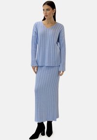 Ensemble composé d'un pull tricoté côtelé bleu clair et d'une jupe longue avec un décolleté en V, manches longues et ourlet légèrement court. Bottines noires.