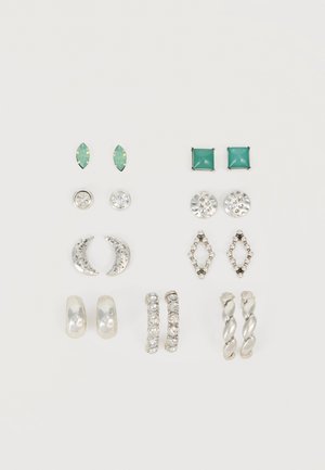 Six paires de boucles d'oreilles argentées et vertes, à clous et anneaux, disposées en deux colonnes verticales sur fond blanc.