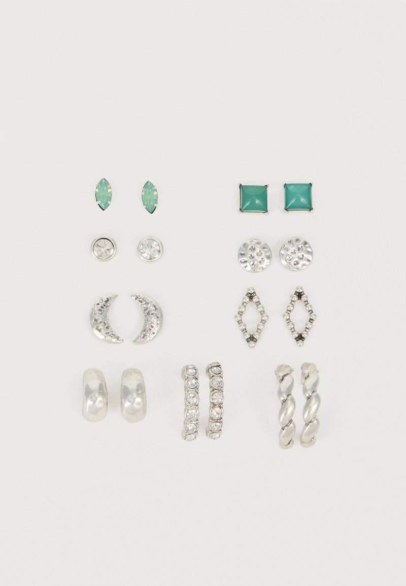 Six paires de boucles d'oreilles argentées et vertes, à clous et anneaux, disposées en deux colonnes verticales sur fond blanc.