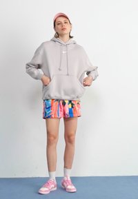 Ljust grå huvtröja med dragsnoddar; färgglada mönstrade shorts med blå och rosa ränder; rosa sneakers och strumpor.