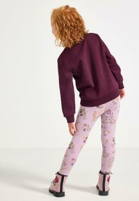 Lilla sweatshirt med ribbede manchetter, parret med lyserøde leggings med blomsterprint i forskellige farver. Sorte og lyserøde ankelstøvler.