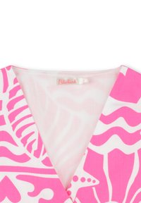 Haut en tissu blanc avec des motifs abstraits roses audacieux, présentant un décolleté en V profond et une étiquette indiquant "Billieblush". Texture légère et lisse.