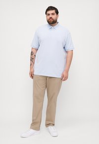 Tricou polo albastru deschis cu guler standard, mâneci scurte și croială lejeră, asociat cu pantaloni chino bej și adidași albi.