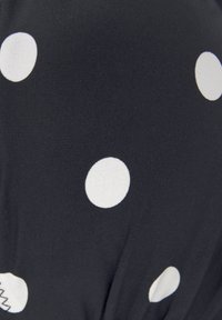 Zwarte stof met grote witte stippen. De textuur is glad met subtiele ribbels, en toont een ontspannen, geplooid ontwerp.