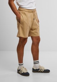 Beige bomullsshorts med elastisk midje, snor, to sidelommer og subtile sømdetaljer. Kombinert med marineblå sneakers og stripete sokker.