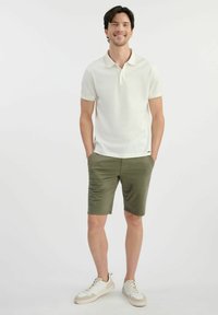 Biała koszulka polo z delikatnym wzorem kołnierza, w połączeniu z oliwkowymi szortami i białymi butami z beżowymi akcentami.