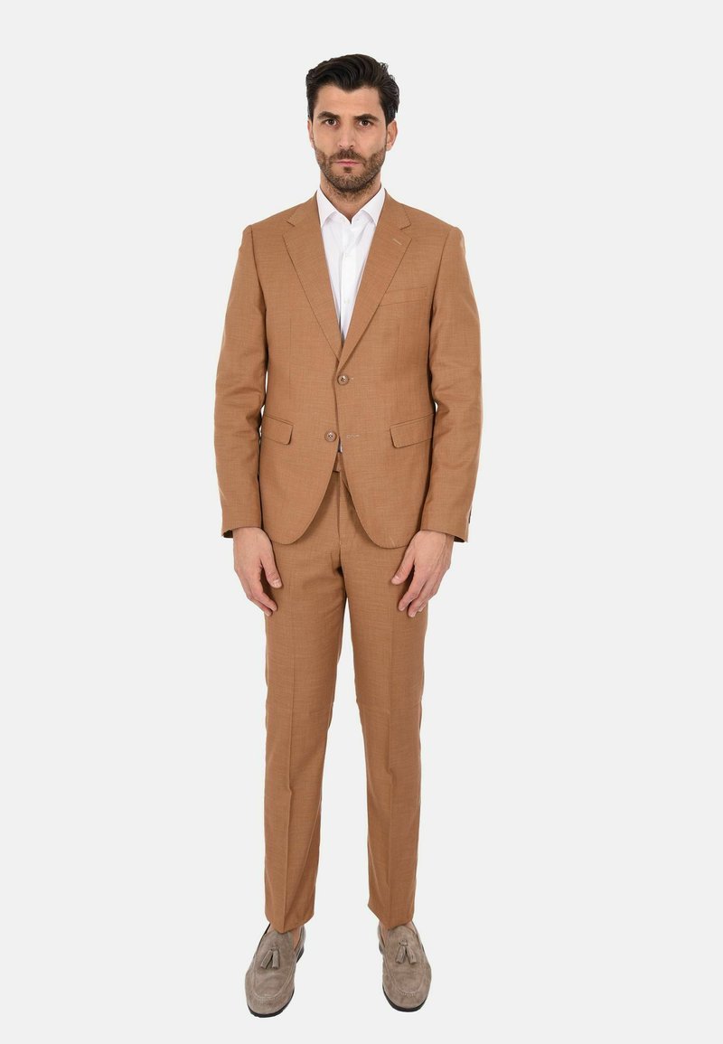 Completo beige con un taglio su misura, tessuto morbido, giacca monopetto, revers a notcher e pantaloni abbinati, abbinato a una camicia bianca.