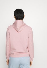 Sudadera con capucha rosa hecha de material suave, con capucha ajustable con cordón, puños acanalados y un corte holgado, combinada con pantalones azul claro.