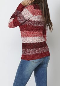 Sweter dziany w pionowe czerwone i białe paski, teksturowany materiał i ściągacze przy mankietach. W połączeniu z dopasowanymi niebieskimi dżinsami.