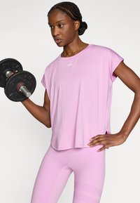 Ροζ αθλητικό τοπ με κοντά μανίκια, που διαθέτει στρογγυλή λαιμόκοψη και πλευρικές σχισμές. Συνδυάζεται με ροζ κολάν στο ίδιο χρώμα και αλτήρα.