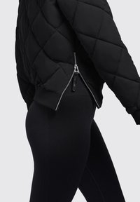 Zwarte gewatteerde pufferjack met geribde manchetten en een zijrits. Gecombineerd met hoogwassende, gestructureerde zwarte leggings.