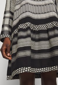 Schwarz-weiß gestreiftes Kleid mit aufwendigen Webmustern, ausgestelltem Rock und langen Ärmeln. Reiche Textur mit vielfältigen Linienmustern.