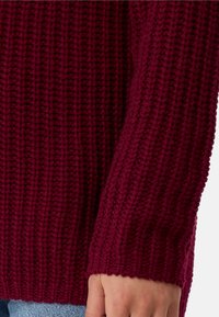 Bordeaux gebreide trui, voorzien van een gestructureerd ribpatroon, met een losse pasvorm en een brede manche die een deel van de hand bedekt.