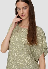 Blouse à motifs vert clair avec une coupe décontractée, ornée de pois blancs irréguliers, à manches courtes et col arrondi.
