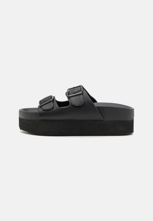 Black platform sandals made of smooth material, featuring two adjustable straps with buckles, and a textured sole for grip.