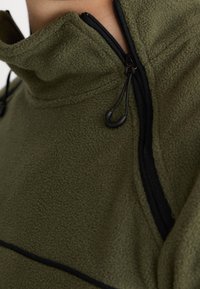 Close-up of green fleece jacket with black zipper and adjustable drawstring cord near the neck and shoulder area.