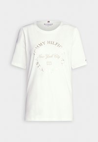 Camiseta de algodón blanca con un gráfico redondo que presenta "Tommy Hilfiger", "Nueva York" y "EST. MCMXC" en bordado beige. Mangas cortas.