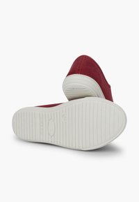 Scarpe di tela rosse con punta arrotondata e suola in gomma bianca. Presentano dettagli di cucitura lungo il bordo superiore e una suola testurizzata per una migliore aderenza.