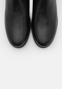 Bottes noires en cuir à la cheville avec bouts ronds, texture lisse et coutures minimales. Semelles robustes et design épuré et moderne.