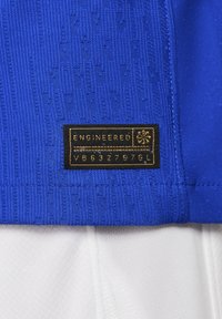 Jersey deportivo azul con tejido texturizado, parche con el logo que dice "ENGINEERED" en dorado y acentos en blanco en la parte inferior.