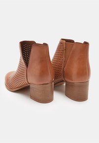 Brązowe botki za kostkę wykonane z gładkiej skóry z perforowanym wzorem. Krótki, warstwowy obcas i boczne elastyczne panele ułatwiające zakładanie.