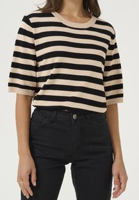 Stribet striktrøje i beige og sort, korte ærmer, rund halsudskæring, blød tekstur. Kombineret med sorte slim-fit jeans, metalknapdetalje.
