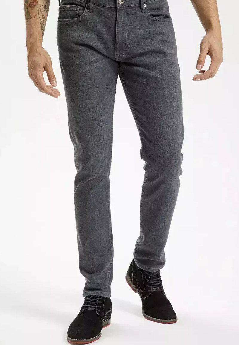 Szare dżinsy o slim fit, z pięcioma kieszeniami i zapięciem na guziki, w połączeniu z czarnymi zamszowymi butami z zielonymi i czerwonymi akcentami.