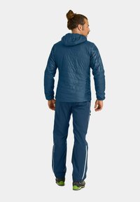 Marineblaue isolierte Jacke mit Kapuze und gepolstertem Muster, kombiniert mit passenden Hosen mit reflektierenden Akzenten und einer lockeren Passform.