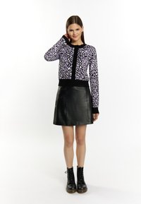 Cardigan a stampa leopardata viola con dettagli neri, abbinato a una gonna in pelle nera. La modella indossa stivali neri con lacci.