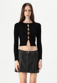 Haut court noir à côtes avec des manches longues et un détail en trou de clé à l'avant ; associé à une mini-jupe en cuir noir avec des coutures contrastées.