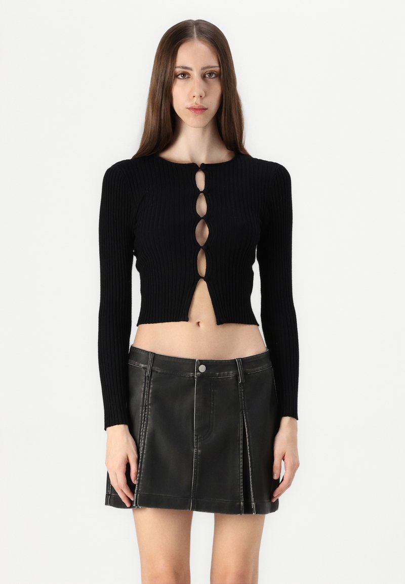 Haut court noir à côtes avec des manches longues et un détail en trou de clé à l'avant ; associé à une mini-jupe en cuir noir avec des coutures contrastées.