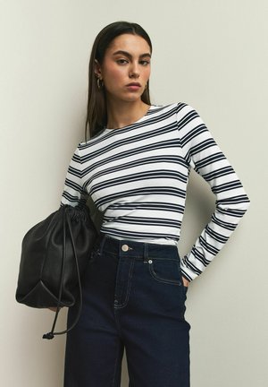 Long-sleeve shirt with black and white horizontal stripes, made of a soft fabric. Paired with high-waisted dark jeans and a black drawstring bag.