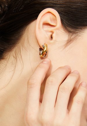 Nahaufnahme eines Ohrs, das einen gedrehten Gold- und Silberreifenohrring trägt, wobei Finger sanft das Ohrläppchen berühren.