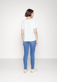 White cotton t-shirt with short sleeves, casual fit, paired with light blue skinny jeans and beige sneakers with a textured sole.