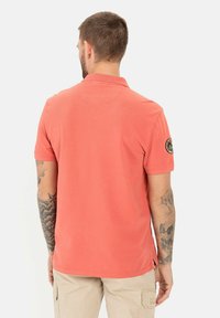 Koraalkleurig polo-shirt met korte mouwen, textuurstof en zijsplitten. Bevat een logo-patch op de linker mouw en een klassieke kraag.