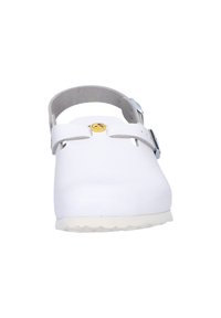 White clogs with a smooth plastic exterior, a round toe, adjustable heel strap, and a yellow logo accent on the front.