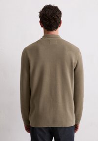 Olijfgroene gebreide trui met een relaxed fit, lange mouwen en een gestructureerde afwerking. Heeft een kleine kraag en een zoom die lichtjes naar buiten buigt.