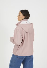 Veste à capuche rose avec doublure blanche, offrant une coupe décontractée, un tissu lisse et des poches latérales inclinées. Portée sur un jean bleu.