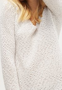 Lekki biały sweter dziany z dekoltem w kształcie litery V, teksturowanym wzorem i długimi rękawami, oferujący swobodny i przewiewny design.