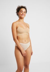 Reggiseno seamless beige chiaro con spalline sottili e finitura liscia, abbinato a mutande a vita alta coordinate. Entrambi hanno una texture morbida e elastica.