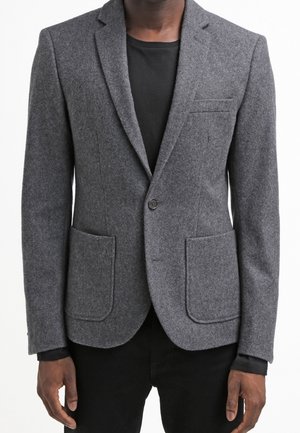 Blazer en mélange de laine gris avec revers crantés, fermeture à un bouton, et deux poches plaquées à l'avant. Texture lisse et coupe ajustée.