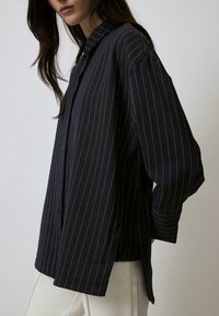 Navy striped button-up shirt with a relaxed fit, featuring long sleeves, a pointed collar, and side slits for ease of movement.