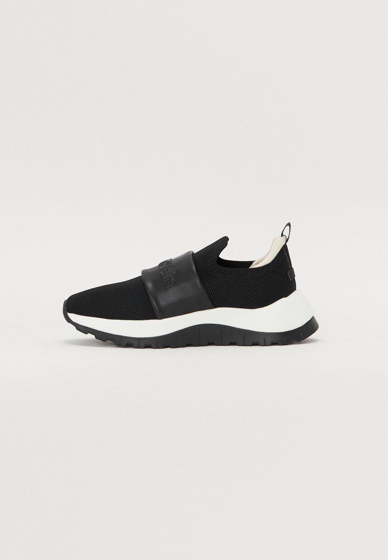 Baskets noires slip-on avec semelle blanche épaisse, empeigne tricotée, large bande élastique sur le médio-pied et languette au talon.
