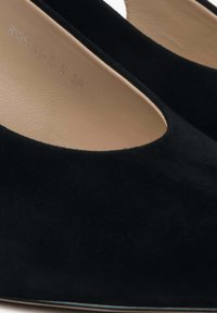 Zwarte suède pumps met een ronde neus en open zijkanten, voorzien van een beige inlegzool. De hak is een stijlvolle, gepolijste zwart. Eenvoudig en elegant ontwerp.