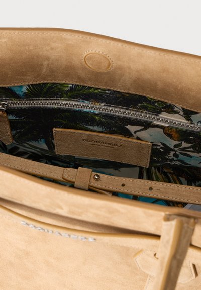 Τσάντα από μπεζ σουέντ με εσωτερική τσέπη με φερμουάρ, που διαθέτει ζωηρή φόδρα με μοτίβο φοινικόδεντρων. Περιλαμβάνει επίπεδη δερμάτινη ετικέτα και λεπτομέρεια στο λουρί.